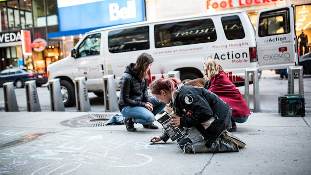 Des jeunes dessinent avec une craie des dessins à même le sol sur la rue Sainte-Catherine à Montréal