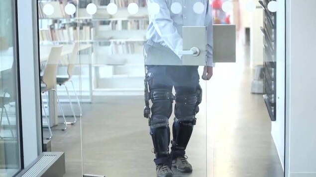 Un homme porte des prothèses intelligentes aux jambes et marche pour ouvrir une porte.