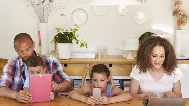 Deux parents et deux enfants regardant leur téléphone ou leur tablette. 
