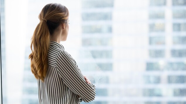 Une femme regarde à l'extérieur d'une fenêtre d'une tour à bureau.