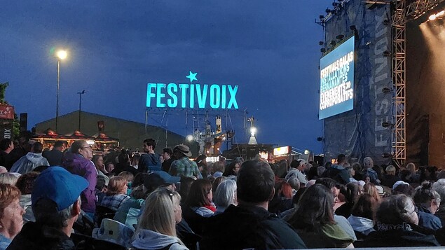 Une enseigne lumineuse du FestiVoix de Trois-Rivières et une foule devant une scène.