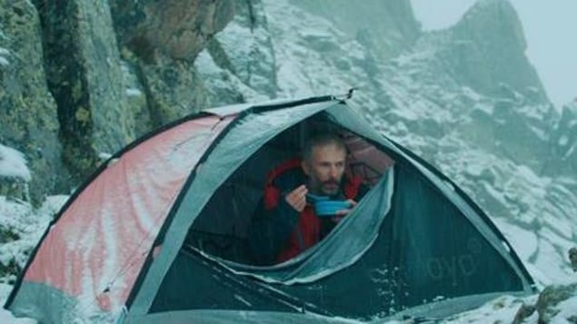 Un homme campe sous une tente dans la montagne enneigée