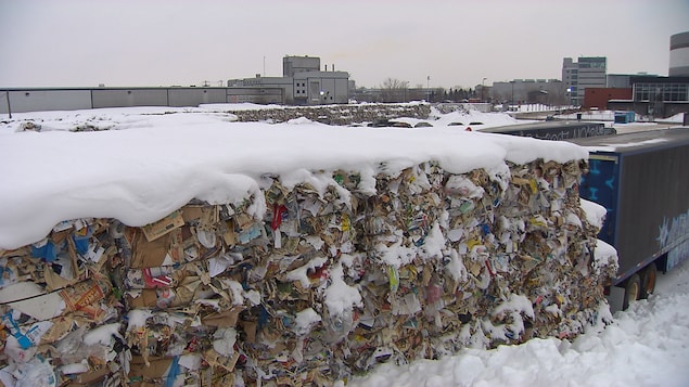 Des ballots de matières recyclables dans la neige derrière des camions, près d'un centre de recyclage à Montréal, en janvier 2018.