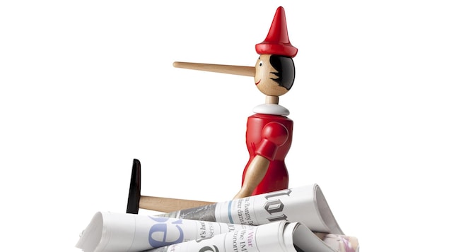 Un Pinocchio assis sur une pile de journaux pour représenté les Fake News.