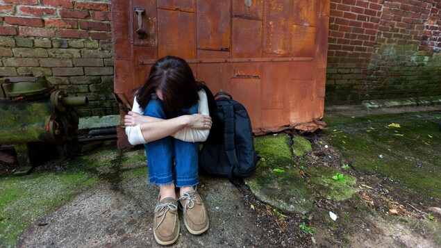 Une jeune fille en fugue est assise par terre devant une porte.