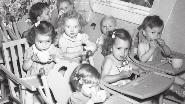 Huit enfants qui mangent assis dans des chaises hautes.