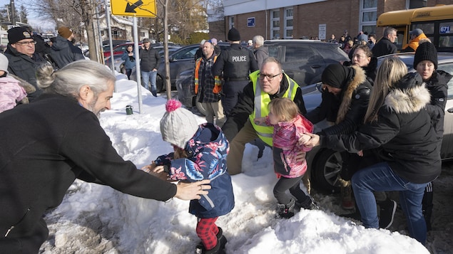 Des adultes aident des bambins à franchir un banc de neige devant une école.