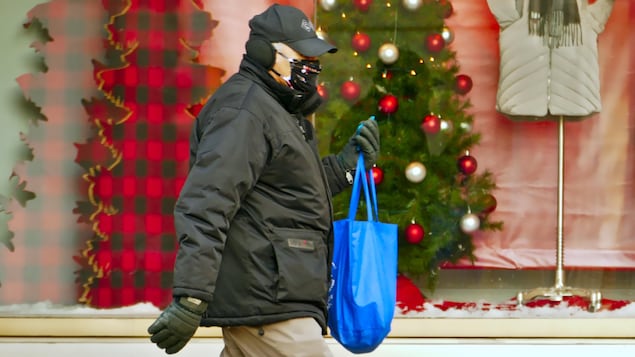 Un homme, un sac de magasinage à la main, porte un masque à l'extérieur pendant la pandémie de COVID-19 en hiver.