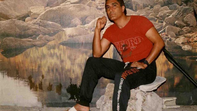Il porte des sandales blanches, un chandail rouge et un pantalon noir.