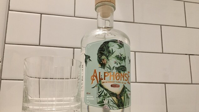 Une bouteille de gin avec une étiquette verte à côté d'un verre vide.
