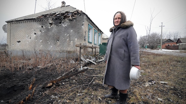 Una mujer junto a una casa bombardeada.