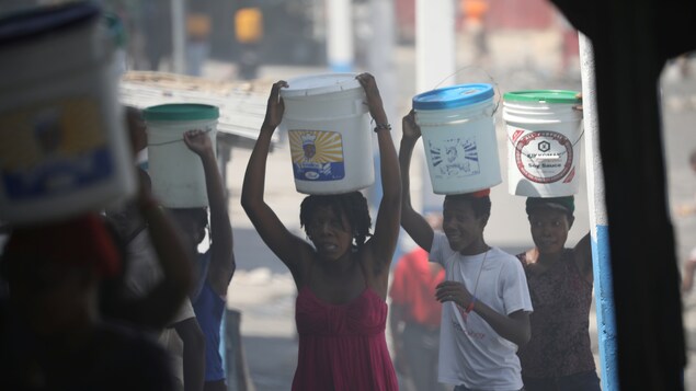 Hommes et femmes transportant des seaux sur leur tête dans les rues bloquées de Port-au-Prince. Hommes et femmes transportant des seaux sur leur tête dans les rues bloquées de Port-au-Prince.