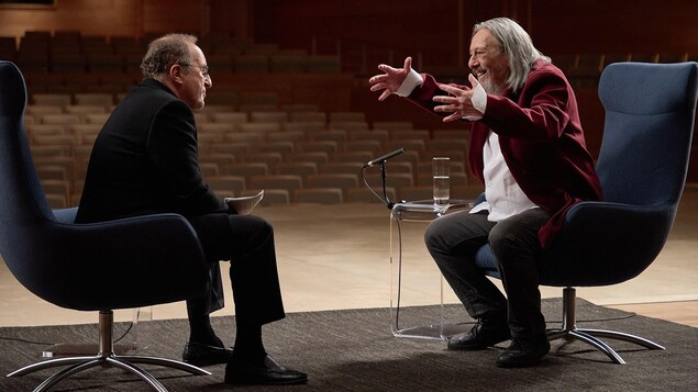 L'animateur Bernard Derome et l'auteur-compositeur-interprète Serge Fiori sont assis sur la scène de la Maison symphonique de Montréal.