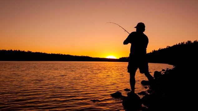 Un pêcheur s'exerce au petit matin devant un lac.