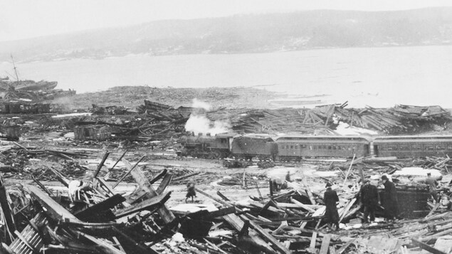 Photo de l'après-explosion montrant la dévastation, ainsi qu'un train en arrière-plan. Photo de l'après-explosion montrant la dévastation, ainsi qu'un train en arrière-plan.