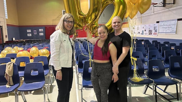 La directrice Debra Muchnik, l'élève Noémie D'Aigle Edwards et sa mère Nadine D'aigle tiennent un ballon 100e anniversaire dans le gymnase de l'école Heydon Park. 