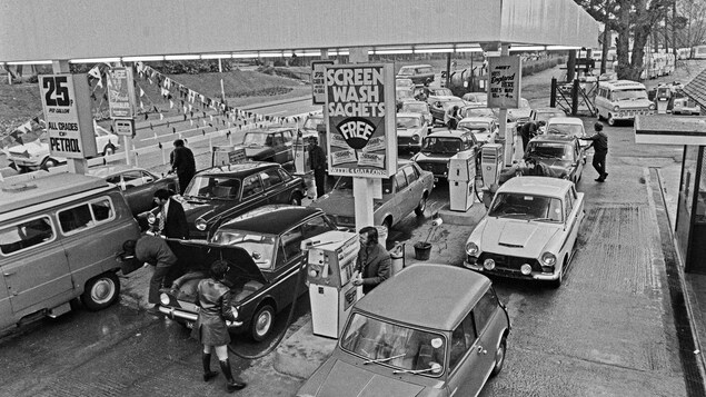 Un grand nombre de voitures se trouvent dans un poste d’essence où des personnes remplissent leur réservoir.