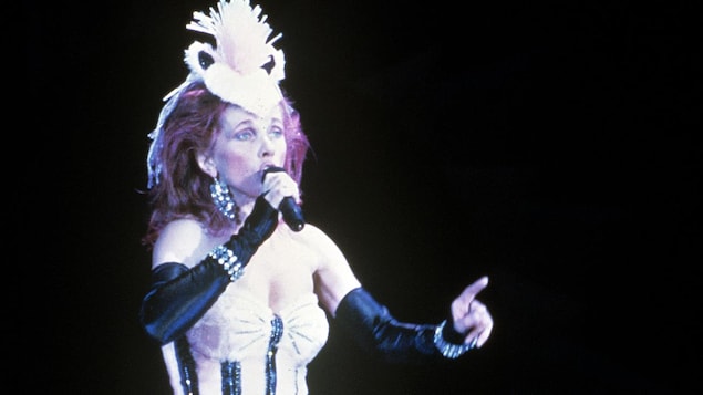 Une chanteuse habillée en costume et portant une coiffe sur la tête est sur scène.
