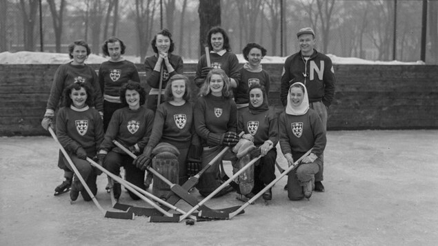 Une équipe de hockey féminin et leur entraîneur pose pour une photo officielle sur une patinoire.