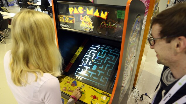 Une femme joue à une version arcade du jeu Pac-Man, tandis qu'un homme la regarde en souriant.