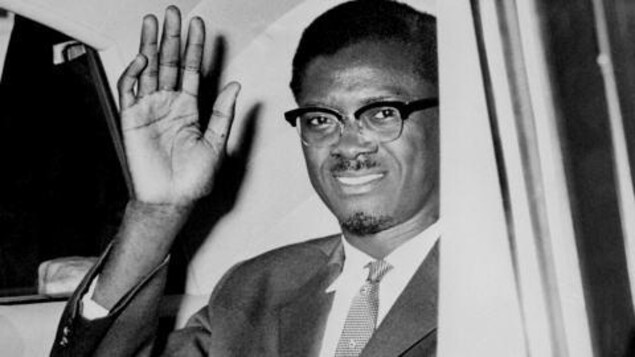 Assis dans une voiture, Patrice Lumumba salue de la main.