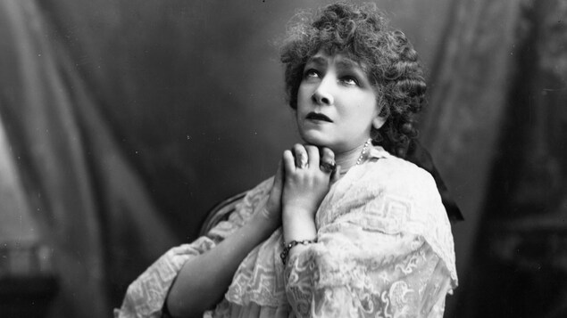 Sarah Bernhardt est assise de côté, les mains jointes.