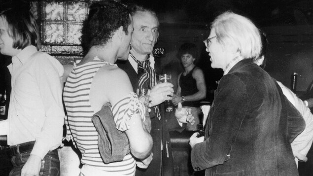 À droite, l'artiste visuel Andy Warhol discute avec deux hommes au Studio 54.