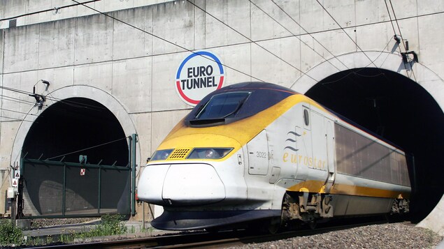 Un train jaune et blanc nommé Eurostar sort d'un tunnel qui porte le nom d'Eurotunnel.