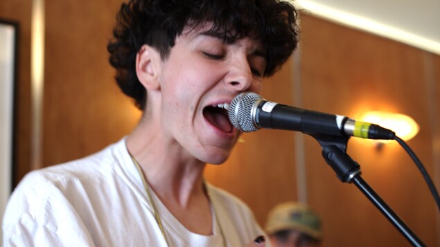 Hubert Lenoir chante, la bouche ouvert, dans un micro sur un pied.
