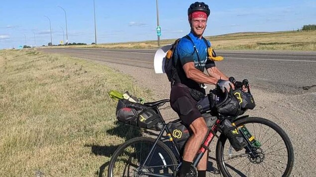 Hugo Lambert assis sur son vélo au bord d'une autoroute en Saskatchewan. 