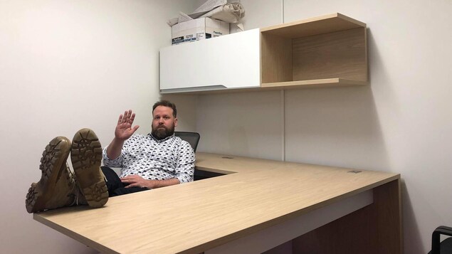 Hugo Meunier pose dans un bureau vide en faisant un signe d'au revoir de la main.