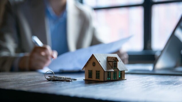 Unas llaves y una casa sobre la mesa delante de una persona que firma papeles.