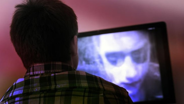 Un jeune homme regarde un film d'horreur à la télévision. 