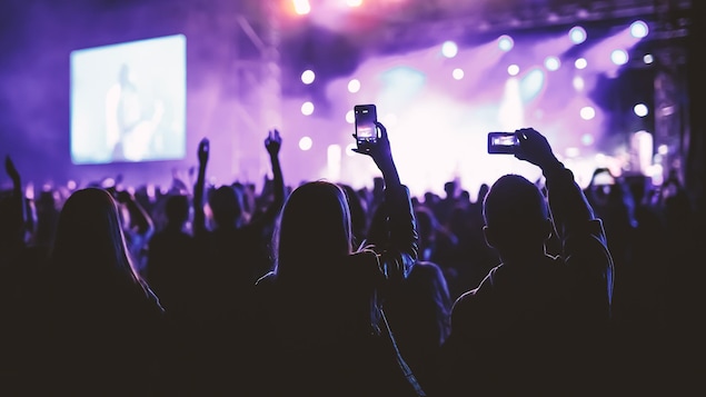Des gens dans une foule tenant un téléphone intelligent devant un concert.