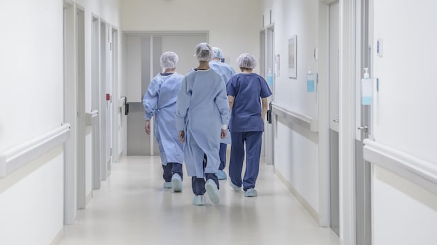 Quatre employés médicaux marchent de dos dans un couloir d'hôpital.
