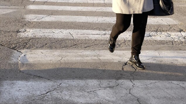 Une femme traverse une rue sur un passage piétonnier. 