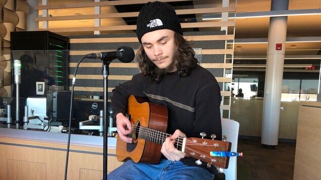Jacques Surette assis sur un tabouret et jouant de la guitare.