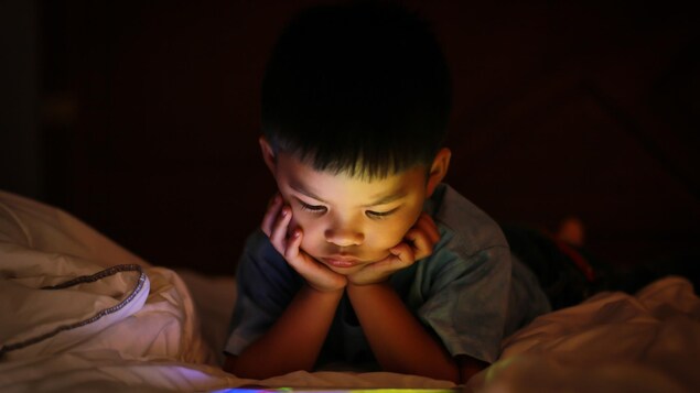 Un jeun enfant regarde une tablette le soir.