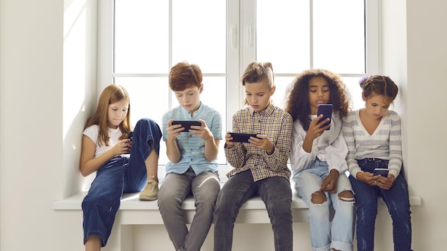 Des enfants sont assis au bord d'une fenêtre et consultent leur téléphone.