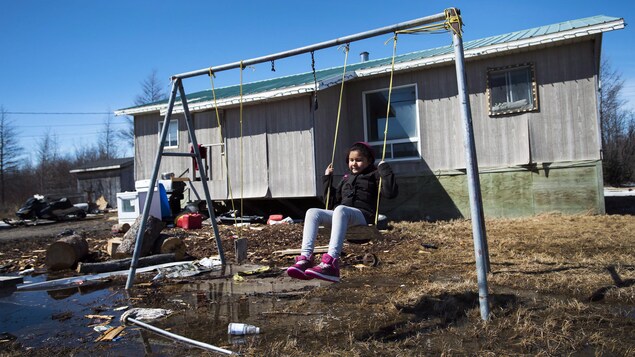 Une enfant joue sur une balançoire à l'arrière d'une maison dans une cour jonchée de déchets.
