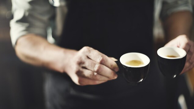 Gros plan sur les mains d'un serveur tenant deux petites tasses de café.