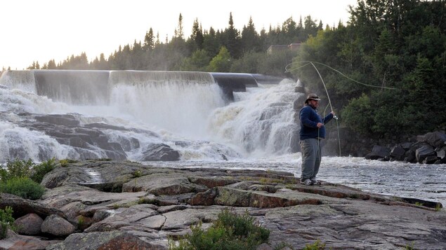 Le pêcheur nord-côtier Jocelyn LeBlanc entrain de pêcher à la mouche sur une rivière au pied d'un barrage hydroélectrique.