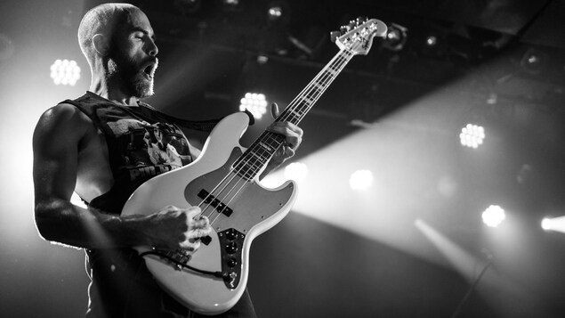 Josh McLeod joue une basse sur scène et la photo est en noir et blanc.