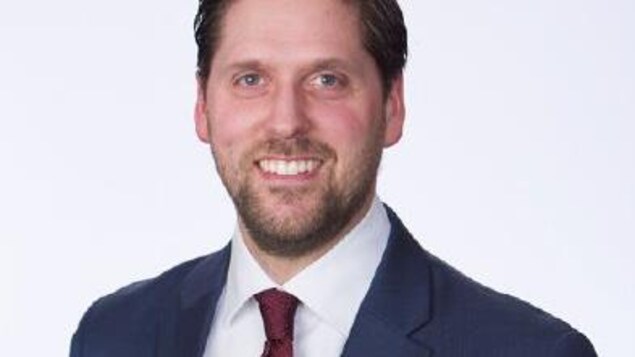 L'avocat Justin E. Kingsway porte un veston bleu, une cravate rouge et une chemise blanche.