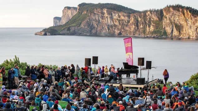 Des spectateurs entourent une scène extérieure sur laquelle une personne interprète une pièce sur un piano à queue au lever du soleil dans un parc national.