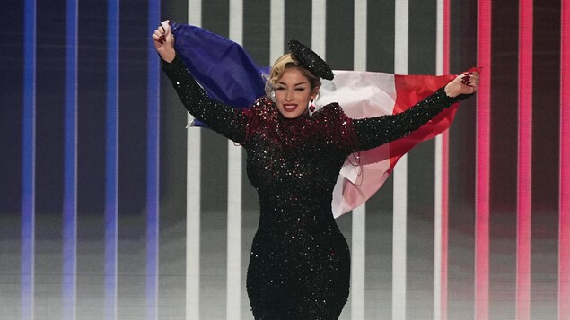 Une femme vêtue d'une robe à paillettes étincelante porte un drapeau de la France à bout de bras lors de son entrée sur scène. 