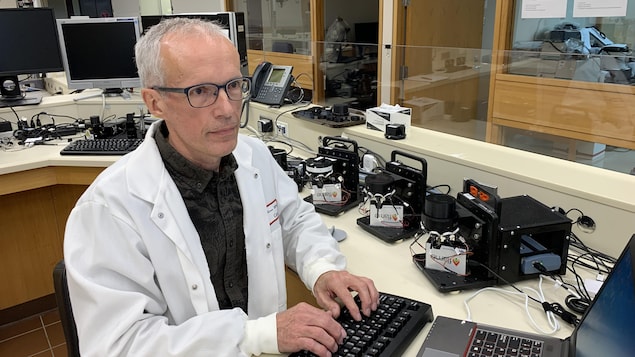 Un chercheur, dans la cinquantaine et portant des lunettes, entouré de plusieurs instruments scientifique dans son laboratoire, regarde des données qui apparaissent sur un écran d'ordinateur.