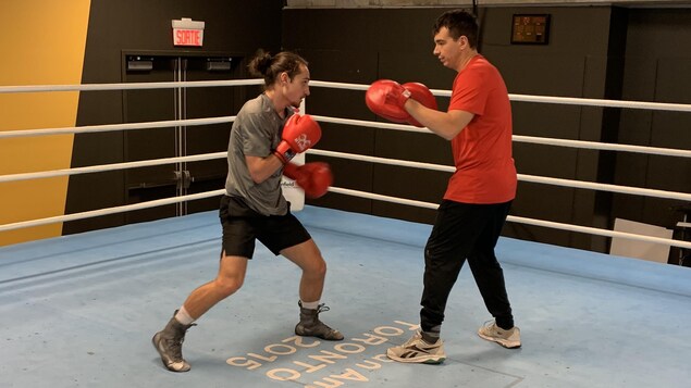 Un jeune boxeur et son entraîneur s'échangent des coups au milieu d'un ring, lors d'un exercice.