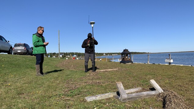 Des responsables du Ministère des Ressources naturelles du Nouveau-Brunswick prennent des relevés à l'aide d'une borne GPS sur un terrain près de la mer.