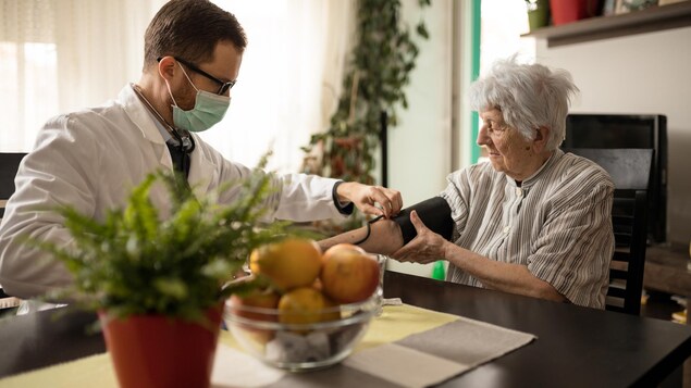 Un infirmer portant un masque mesure la pression artérielle d'une personne âgées à l'aide d'un brassard de tensiomètre.